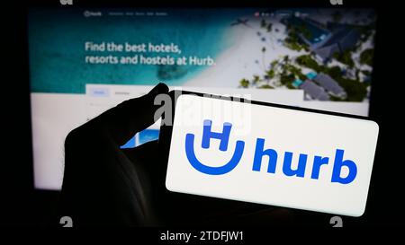 Person mit Smartphone und Logo des brasilianischen Reiseunternehmens Hurb Technologies S.A. vor der Website. Schwerpunkt auf dem Display des Telefons. Stockfoto