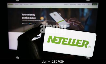 Person mit Smartphone und Logo des globalen Zahlungsplattform-Unternehmens Neteller vor der Website. Schwerpunkt auf dem Display des Telefons. Stockfoto