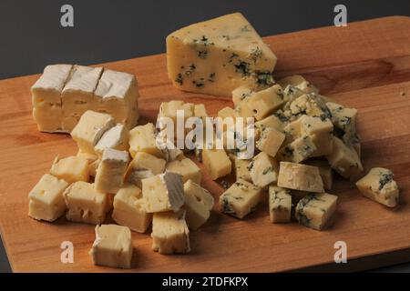 In Scheiben geschnittene Käsestücke auf einem Holzbrett auf grauem Hintergrund Stockfoto