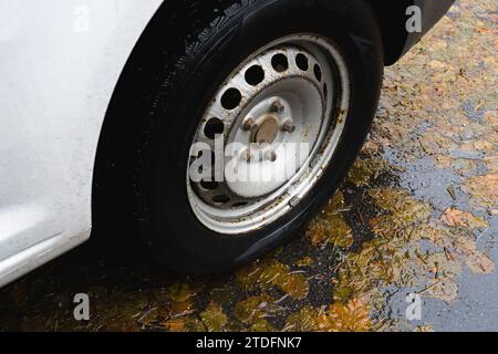 Nahaufnahme des Autoreifens auf nassem Asphalt, der im Herbst mit gelben Blättern bedeckt ist. Stockfoto
