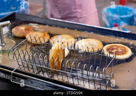 Hotteok zum Verkauf und die Hände eines Händlers, der es auf einer Straße auf einem traditionellen Markt in Korea grillt Stockfoto