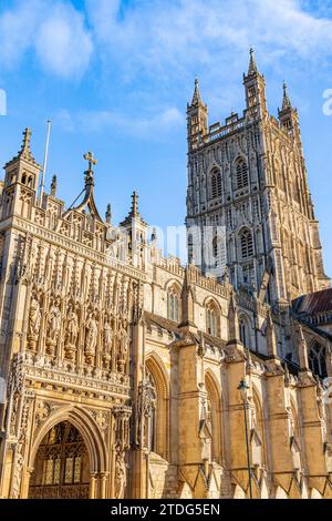 Morgensonnenlicht auf der wunderschön geschnitzten Veranda und dem dekorierten Turm aus dem 15. Jahrhundert der Kathedrale von Gloucester, Gloucester, Großbritannien, mit Blick auf eine blaue Ske Stockfoto