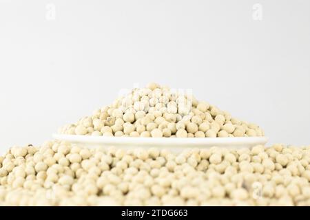 Weißer Pfeffer in einer weißen Schüssel auf einem Stapel weißer Paprika, isoliert auf weißem Hintergrund. Stockfoto