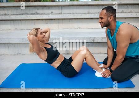 Frau, die an Sit-UPS arbeitet, während der persönliche Trainer Hilfe leistet. Stockfoto