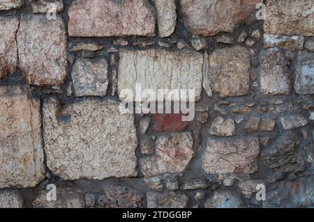 Ein Teil einer alten, europäischen Steinmauer, die mit kleinen und großen Steinen in verschiedenen Farben und Texturen gebaut und mit Zementfugen zusammengehalten wurde. Stockfoto