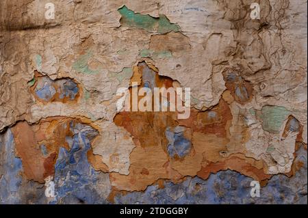 Abstrakt, Detail, Muster eines Abschnitts aus mehrfarbigen, blauen, ockerfarbenen, gelben und braunen abblätternden Farbschichten auf einer alten Steinaußenwand eines Wohnhauses Stockfoto