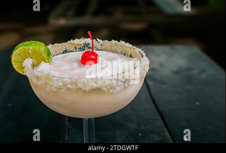 Nahaufnahme von köstlichem gefrorenem Kokoscocktail mit Kirsche. Gefrorene Kokosnuss-Margarita mit Zitronenscheibe, serviert auf Holztisch Stockfoto