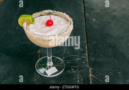 Gefrorene Kokosnuss-Margarita mit Zitronenscheibe, serviert auf Holztisch. Nahaufnahme von köstlichem gefrorenem Kokoscocktail mit Kirsche Stockfoto