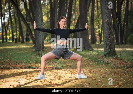 Sportliche Frau, die an einem warmen, sonnigen Tag im Park steht, Rudrasana, eine Kraft-Asana zur Stärkung der Beinmuskulatur Stockfoto