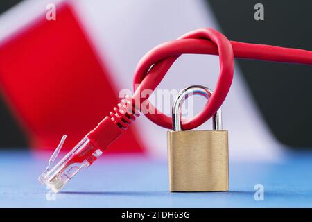 Ein geschlossenes Schloss auf einem gekoppelten Netzwerkkabel in einen Knoten vor dem Hintergrund der polnischen Flagge, dem Konzept der Sicherheit der Internet-Technologien in Polen Stockfoto