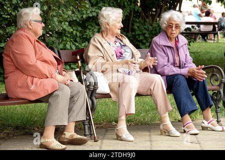 Drei alte Damen diskutieren. Rentner sitzen auf einer Bank in einem Stadtpark Ruhestand, ältere Generation, alte Leute, Senioren Lebensstil, alternde Bevölkerung Stockfoto