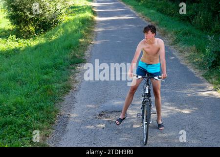 Junger Mann allein 20 auf einem Fahrrad auf einer Landstraße, Sommer, nur in kurzen Hosen Fahrrad ohne Helm fahren, heißes Wetter Stockfoto