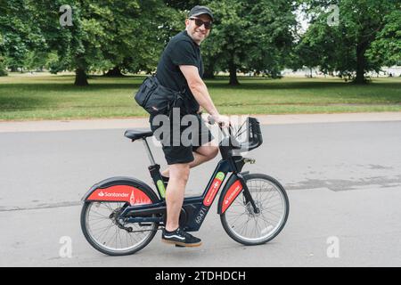 Ein Mann fährt mit einem Leihfahrrad/Verleih-Santander eBike in London durch einen Park Stockfoto