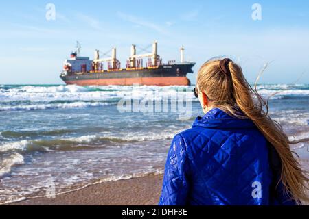 Frau schaut auf das große Frachtschiff Blue Shark, das vor der Küste des Schwarzen Meeres auf Grund gelaufen ist. Vitjasevo, Russland-02,12,2023 Stockfoto