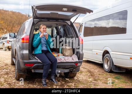 Eine reife Frau hatte ein Picknick im Kofferraum ihres Autos. Roadtrip in die Berge im Herbst. Stockfoto