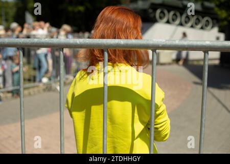 Das Mädchen steht hinter dem Zaun. Details zum Stadtereignis. Zaun von Passanten. Stahlzaun. Stockfoto