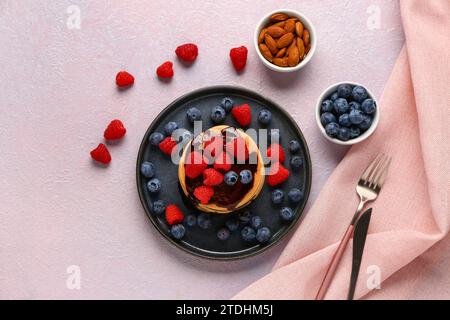 Teller mit süßen Pfannkuchen, Beeren und Nüssen auf pinkfarbenem Hintergrund Stockfoto