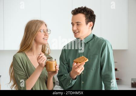 Junge Frau mit Nussbutter in der Hand und hübscher Mann mit Toast in der Küche Stockfoto