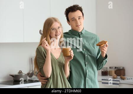 Junge Frau mit Nussbutter in der Hand und hübscher Mann mit Toast in der Küche Stockfoto