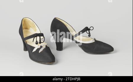 High-Heels-Schuhe mit gewellten Bändern, ca. 1930 Damenschuh aus schwarzem Satin. Modell: Abgerundete Nase, ein Deckblatt und zwei Seitenbleche. Die Seitenbleche und die Deckblätter kommen am Geleng zusammen. Von diesem Punkt an laufen zwei Reifen über den Riegel. Die Reifen werden durch ein schwarzes Seil mit zwei Wulsten zusammengehalten. Die Vorderseite der Ferse verläuft in einem abgerundeten Winkel gerade nach unten. Die Seite und Rückseite der Ferse sind leicht geschnitten und mit schwarzem Satin bedeckt. Achlap aus schwarzem Leder mit fünf Nägeln an der Ferse und schwarzer Ledersohle. Mit elfenbeinfarbenem weißem Leder gefütterte Seitenlaken. Mit Elfenbein bedeckt Stockfoto