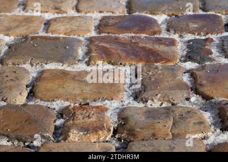 Kopfsteinpflaster, fotografiert von schräg oben. Es liegt Schnee in den Gelenken. Es besteht Rutschgefahr. Stockfoto