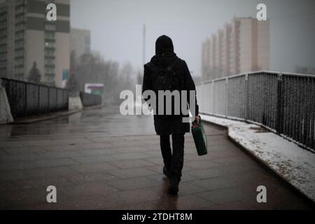 Ein Typ mit Diplomat läuft die Straße runter. Mann in schwarzer Kleidung in der Stadt. Bewölktes Wetter am Nachmittag. Person geht durch die Fußgängerzone. Stockfoto