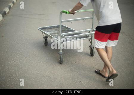 Der Typ schiebt den Wagen. Ein Mann trägt einen leeren Wagen. Lader auf der Straße. Transportwagen zum Transport kleiner Lasten. Stockfoto