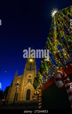 Der Weihnachtsbaum von Għajnsielem erhebt sich in den Abendhimmel neben der neogotischen Pfarrkirche Unserer Lieben Frau von Loreto auf dem Pjazza Madonna Ta' Loreto in Mġarr auf der Insel Gozo, Malta; übergroße Zuckerstangen schmücken seinen Sockel. Der 60 Fuß hohe (rund 18 Meter) Baum, aus Eisen gefertigt, ist mit 5.000 beleuchteten Glasflaschen geschmückt und wurde 2021 zu Europas schönstem Weihnachtsbaum gekürt. Stockfoto
