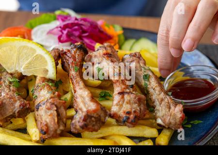 Nahaufnahme des Tellers mit gegrillten Sparerippchen mit Pommes frites und Salat mit weiblicher Hand Stockfoto