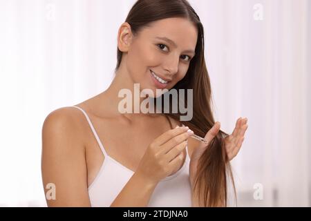 Schöne Frau, die drinnen Serum auf die Haare aufträgt Stockfoto