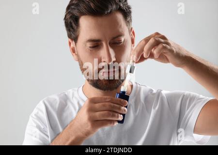 Schöner Mann, der kosmetisches Serum auf hellgrauem Hintergrund öffnet Stockfoto