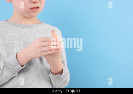 Kleiner Junge, der Pflaster auf den Finger vor hellblauem Hintergrund klebt, Nahaufnahme. Leerzeichen für Text Stockfoto