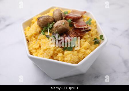 Gekochtes Maismehl mit Speck, Pilzen und Mikrogrün in Schüssel auf weißem Marmortisch, Nahaufnahme Stockfoto