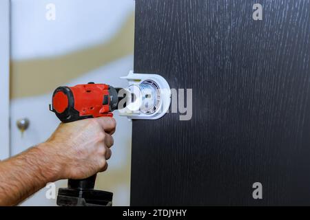 Bohren von Löchern für Schlossgriffe in Holztüren durch Handwerker Stockfoto