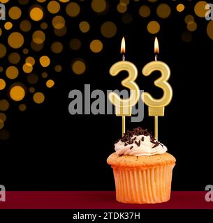 Nummer 33 Geburtstagskerze - Cupcake auf schwarzem Hintergrund mit unscharfen Lichtern Stockfoto