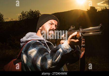 Bärtiger Jäger, der eine Waffe hält und im Wald läuft. Rifle Hunter Silhouette im wunderschönen Sonnenuntergang. Autunm Jagen. Bergjagd. Lauf einer Pistole. Stockfoto