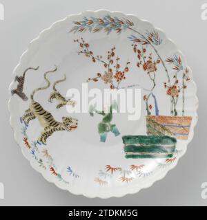 Saucer-dish with bamboo, prunus, tiger and a Chinese boy, anonymous, c. 1700 - c. 1724 Scale of porcelain with a ribbed wall and lobed edge, painted on the glaze in blue, red, green, yellow, black and gold. On the front a dancing Chinese boy between three tigers on one side and bamboo and prunus branch behind hedges on the other. Famle Verte in the Japanese Kakiemon style. NB: broken in box. China porcelain. glaze. gold (metal) painting / gilding / vitrification Scale of porcelain with a ribbed wall and lobed edge, painted on the glaze in blue, red, green, yellow, black and gold. On the front Stockfoto