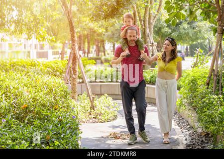 Glückliche Familie zusammen spazieren im öffentlichen grünen Park junger Junge, der auf der Schulter des Vaters um frische ökologisches Bäume herum sitzt. Stockfoto