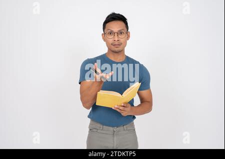 Ein kluger, seriöser asiatischer Mann steht auf einem isolierten weißen Atelierhintergrund mit einem Buch und einem Stift in der Hand. Stockfoto
