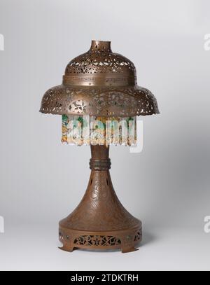 Dämmerung mit Ajour-Motiven, Theo Nieuwenhuis, in oder vor ca. 1914 die Lampe wurde aus vielen Teilen zusammengestellt. Diese sind mit geätzten und sorgfältigen oder ausgeschnittenen Rängen versehen oder nicht in der Motorhaube enthalten). Sie haben einen runden Fleckenring auf vier Füßen, ein Stamm, der sich vom Standring bis zur Mitte mit drei vertikalen Rippen verjüngt, zwei in -abgebildete Verbindungsstücke für die Teile der Haube oder eingearbeitete oder eingearbeitete Teile der Haube. Wo diese zusammenkommen, ist auch ein volant kleiner Glasperlen, in denen unter anderem Schmetterlinge und Libellen zu erkennen sind. T Stockfoto