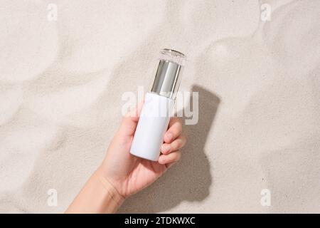 Eine Hand hält eine unbeschriftete Kosmetikflasche auf dem sandigen Hintergrund. Eleganter Raum mit Blick von oben. Kosmetikwerbung. Stockfoto