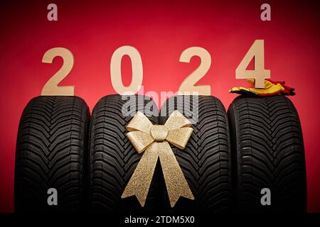 Autoreifen, neue Reifen, Winterräder, goldenes Schleifenband Geschenk, Text 2024 Happy New Year christmas Background. Stockfoto