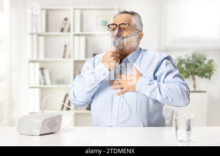 Reifer Mann mit Brustschmerzen mit einem Vernebler zu Hause Stockfoto