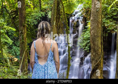 Eine junge Frau in einem Kleid am Kanto Lampo Wasserfall im üppigen tropischen Wald, Bali, Indonesien Stockfoto