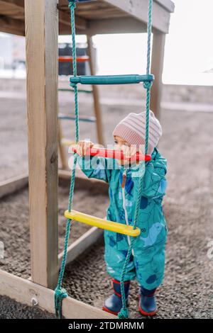 Das kleine Mädchen steht in der Nähe einer Seilleiter und hält sich an einer Holztraverse Stockfoto