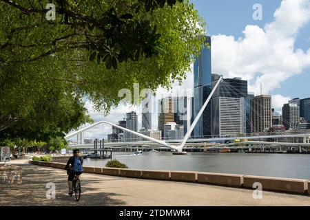 Radfahrer fahren entlang der Clem Jones Promenade, South Bank Parklands, in Richtung Brisbane River, Neville Bonner Bridge und City Skyline Stockfoto