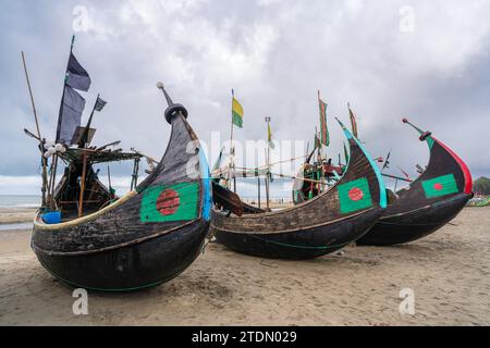Blick auf drei traditionelle hölzerne Fischerboote, bekannt als Mondboote, die am Strand nahe Cox's Bazar in Bangladesch unter bewölktem Himmel ruhen Stockfoto
