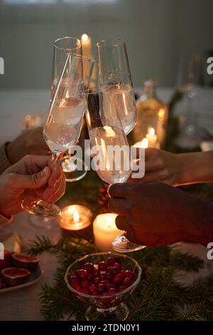 Bei Kerzenschein erleuchtete Hände einer Gruppe von unbekannten Menschen, die Gläser anklitzen, um weihnachten zu feiern Stockfoto