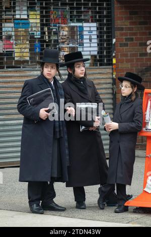 Drei orthodoxe jüdische Jungen, die wahrscheinlich auf dem Weg vom Tempeldienst sind, unterhalten sich in Brooklyn, New York, in einer zwanglosen Straßenecke. Stockfoto