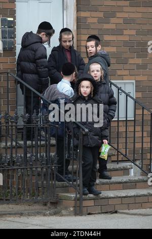 Chassidische jüdische Jungs warten auf ihren Schulbus in Brooklyn, New York. Einige sind in Gesprächen involviert, andere nicht. Stockfoto